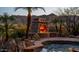 The outdoor stone fireplace with a fire burning sits next to the tranquil backyard pool and landscaping at 12160 E Whispering Wind Dr, Scottsdale, AZ 85255