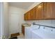 Well-lit laundry room features wood cabinets, washer, dryer and a utility sink by the entry door at 16949 W Oasis Springs Way, Surprise, AZ 85387