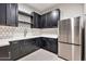 Compact kitchenette features sleek black cabinetry, stainless steel refrigerator, and tiled backsplash at 8730 E Tether Trl, Scottsdale, AZ 85255