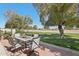 Outdoor patio area with a metal dining table, mature trees, and views of a green space at 11011 N Coggins Dr, Sun City, AZ 85351