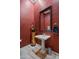 Stylish powder room with dark red textured walls, pedestal sink, and decorative accents at 41711 N Pinion Hills Ct, Anthem, AZ 85086