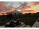 Serene backyard scene featuring lounge seating, manicured lawn, decorative plants, and a large umbrella under a dramatic sunset at 17801 W Mountainair St, Surprise, AZ 85388