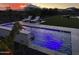 An evening shot of a modern pool featuring fountain features, accent lighting, and poolside lounge chairs and umbrellas at 17801 W Mountainair St, Surprise, AZ 85388