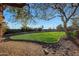 Well-manicured backyard with lush green grass, decorative rock landscaping, and mature trees creating a private oasis at 18919 W Verde Ln, Litchfield Park, AZ 85340