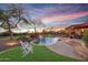 Beautiful swimming pool with a waterfall feature, surrounded by lush landscaping and comfortable seating at sunset at 18919 W Verde Ln, Litchfield Park, AZ 85340
