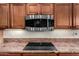 Close-up of a kitchen featuring granite counters, stainless steel microwave and cooktop with wood cabinetry at 6777 S Four Peaks Way, Chandler, AZ 85249