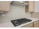 Close-up of a cooktop with stainless steel vent hood, backsplash, and quartz countertops at 13548 W Copperleaf Ln, Peoria, AZ 85383