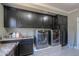 Modern laundry room featuring a sink, dark cabinets, and side-by-side front-load washer and dryer on risers at 1520 E Elmwood Cir, Mesa, AZ 85203