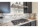 Close-up shot of gas cooktop with stainless steel hood and elegant granite backsplash at 31672 N 135Th Ln, Peoria, AZ 85383