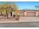 Tan home featuring a three-car garage, desert landscaping, and mature mesquite tree at 3138 W Ravina Ln, Anthem, AZ 85086