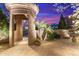 Home's grand entrance with a stone archway, iron gate, and lush landscaping under a colorful sky at 37170 N Granite Creek Ln, Carefree, AZ 85377