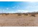 Sprawling desert landscape with distant home featuring a bright blue sky and scattered cloudscape at 53040 W Whirly Bird Rd, Maricopa, AZ 85139