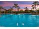 Large community pool with palm trees, sunshades, lounge chairs, and a relaxing waterfall feature at 26828 W Piute Ave, Buckeye, AZ 85396