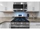 Close up of gas range in a modern kitchen with white cabinets, stainless steel appliances, and granite countertops at 20408 E Rosa Rd, Queen Creek, AZ 85142