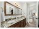 Bathroom featuring a double sink granite vanity, a large framed mirror, and adjacent room view at 3226 E Sells Dr, Phoenix, AZ 85018