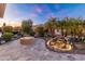Backyard at dusk with a cozy fire pit, rock waterfall, and palm trees at 26648 W Quail Ave, Buckeye, AZ 85396