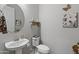 Neutral powder room with a modern round mirror, decorative wall art and a pedestal sink at 26648 W Quail Ave, Buckeye, AZ 85396