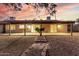 A spacious backyard featuring a covered patio, rock landscaping, and mature palm trees under a sunset sky at 14013 N 57Th Pl, Scottsdale, AZ 85254