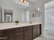 Bathroom featuring a large mirror, double vanity with brown cabinets and a view of a shower room at 14247 W Bronco Trl, Surprise, AZ 85387