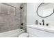 Modern bathroom features sleek gray tiling, a bathtub and shower combo, a dark faucet and a round mirror at 2418 W Flower St, Phoenix, AZ 85015