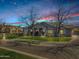 Charming home featuring a well-manicured lawn, mature trees, and a welcoming front entrance, set against a picturesque sunset at 20125 E Melissa Pl, Queen Creek, AZ 85142