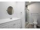 This bathroom features a glass door shower, white cabinets, a round mirror, and wood-look floors at 27227 N 147Th Ave, Surprise, AZ 85387