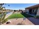 Landscaped backyard with artificial grass, a covered patio, and a waterfront view at 42024 W Rosewood Ln, Maricopa, AZ 85138