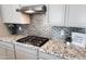 Close up of a kitchen featuring granite countertops, tiled backsplash, and stainless steel hood vent at 42024 W Rosewood Ln, Maricopa, AZ 85138