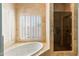 Bathroom with a bathtub near shuttered windows, as well as a glass shower door, and travertine tile at 5345 E Mercer Ln, Scottsdale, AZ 85254