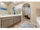 Elegant bathroom featuring double sinks, neutral toned cabinets, and an arched doorway leading to the bedroom at 11627 E Bella Vista Dr, Scottsdale, AZ 85259