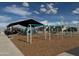 Community playground with swings and play structures under a covered seating area at 17989 W Camino De Oro --, Surprise, AZ 85387