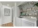 A well-organized laundry room features modern appliances, leafy wallpaper, and built-in storage shelves at 17335 W Cheryl Dr, Waddell, AZ 85355