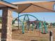 Community playground featuring play structures under a shaded canopy with stone detail on posts at 18334 W Desert Holw Dr, Wittmann, AZ 85361