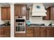 A view of the kitchen shows the stainless steel ovens and the range with a decorative hood vent at 1893 S Sinova S Ave, Gilbert, AZ 85295