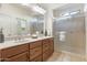Bathroom with dual sinks, wood cabinets, a frameless glass shower, neutral tiling, and decorative accents at 16372 W Mulberry Dr, Goodyear, AZ 85395