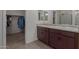 Dual vanity bathroom with dark wood cabinets, framed mirrors, and a walk-in closet nearby at 17583 W Paraiso Dr, Surprise, AZ 85387