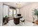 Sophisticated office with a unique chandelier, modern desk, neutral walls, white rug, and view to the front patio at 17336 W Crawfordsville Dr, Surprise, AZ 85388