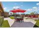 An outdoor dining space has a black table and chairs beneath a red umbrella on a brick patio at 31626 N 129Th Dr, Peoria, AZ 85383