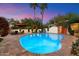 Beautiful backyard pool with lush landscaping, an outdoor fireplace, and comfortable seating under the colorful twilight sky at 7451 E Long Rifle Rd, Carefree, AZ 85377