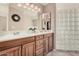 Bright bathroom featuring double sinks, wood cabinets, a large mirror, and a unique glass block shower at 11525 E Laguna Azul Cir, Mesa, AZ 85209