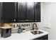 Close-up of the laundry room with dark cabinets, white quartz counters, a stainless-steel sink, and decorative laundry sign at 12539 W Tuckey Ln, Glendale, AZ 85307