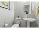 Powder room features a pedestal sink, round mirror, toilet, and artwork at 5189 N 206Th Dr, Buckeye, AZ 85396