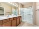 En-suite bathroom featuring dual sinks, wooden cabinets, and a glass-enclosed shower at 18081 W Tasha Dr, Surprise, AZ 85388