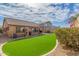 A well-manicured backyard featuring artificial turf, mature shrubs, and a charming playhouse at 25592 W Pioneer St, Buckeye, AZ 85326