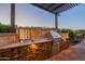 This outdoor kitchen features a stainless steel sink and grill, set in a stone counter beneath a pergola at 706 E La Palta St, Queen Creek, AZ 85140