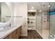 Bright bathroom featuring a wood vanity, glass shelving, and a tiled walk-in shower with pebble accents at 8845 E Sierra Pinta Dr, Scottsdale, AZ 85255