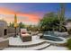 Inviting backyard oasis with a sparkling pool, spa, lounge chairs, and desert landscaping at sunset at 10379 E White Feather Ln, Scottsdale, AZ 85262