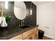 Stylish powder room featuring a black marble accent wall and wooden vanity with brass accents at 9900 N 52Nd St, Paradise Valley, AZ 85253