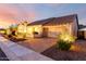 Well-maintained single-story home exterior with a tile roof, warm lighting, a brick-paved driveway, and mature landscaping at 18322 W Thistle Landing Dr, Goodyear, AZ 85338