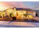 Inviting single-story home with a well-manicured front yard, warm lighting, and a charming entryway, at dusk at 18322 W Thistle Landing Dr, Goodyear, AZ 85338